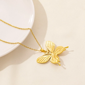 Close-up of golden butterfly pendant necklace resting on white plate and beige fabric