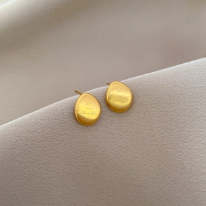 Macro shot of oval gold stud earrings with brushed metal texture and engraved text