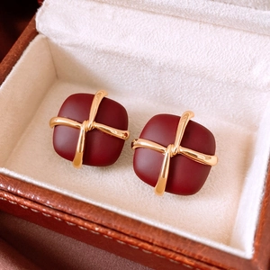 Macro detail of dark red matte square stud earrings with golden cross band design
