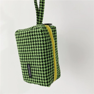 Detail of green houndstooth knit pouch featuring a bright yellow zipper and side label