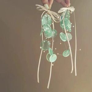 Detail view of handmade earrings featuring green translucent discs and long white silk ribbons