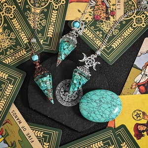Three crystal pendulums with turquoise chips on tarot cards in mystical setting