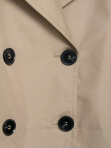 Detail of khaki twill trench coat featuring double-breasted buttons and fabric texture