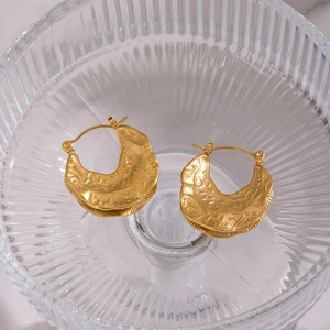 Close-up of golden crescent earrings with hammered texture in a glass dish