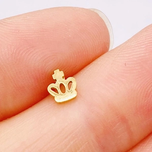 Detailed macro view of a tiny golden crown earring stud on a fingertip for size reference