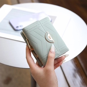 Close-up of light green leather wallet with gold leaf buckle and geometric stitching details