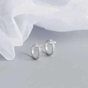 Close-up of a silver cross hoop earring with sparkling stones on a gray background