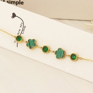 Elegant gold bracelet featuring green gemstone accents and clover leaf charms on white background
