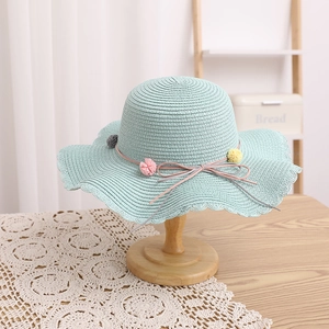 Detail of mint green straw hat featuring colorful pom-poms and elegant wavy brim design
