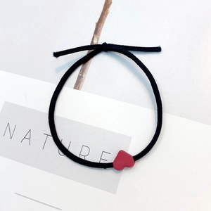 Detail of a black elastic hair tie with a small red heart charm on a modern background