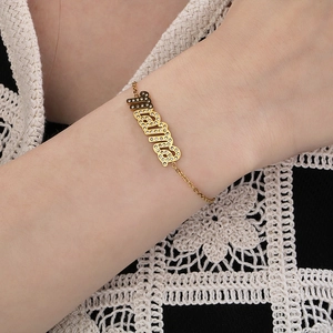 Nahaufnahme des vergoldeten Armbands mit Strass-Namensschild am Handgelenk des Models