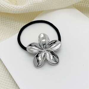Close-up of a black elastic hair tie with a polished silver alloy flower charm on beige fabric