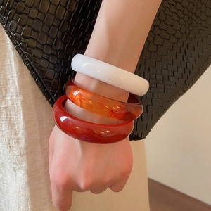 Close-up of three stackable resin bangle bracelets in white, amber, and deep red tones