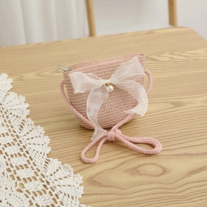 Close-up of pink straw bag with white organza bow and pearl button on wooden table
