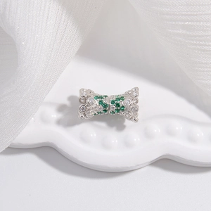 Détail macro d'un charm nœud argenté avec cristaux verts et blancs sur céramique