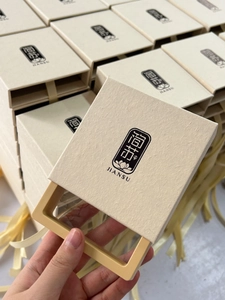 Detalle de la caja de regalo para joyas en color avena con asa amarilla y logo