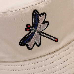 Close-up of colorful dragonfly embroidery on beige cotton canvas bucket hat fabric