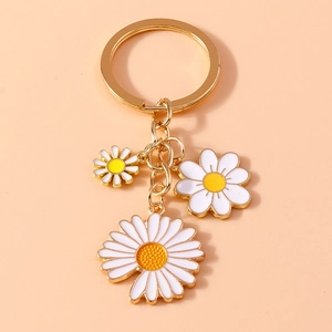 Detailed close-up of golden keychain with white enamel daisy pendants on beige background
