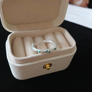 Detail of silver bamboo ring with green enamel leaves on a beige jewelry display box