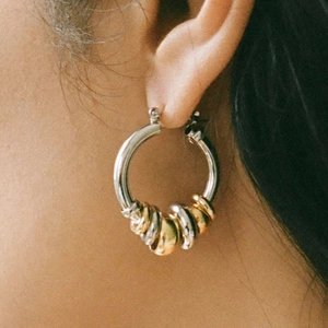 Two-tone stainless steel hoop earrings with gold and silver accents worn by a model