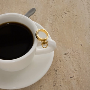 Close-up of golden equestrian ring with pendant hanging on a white coffee cup handle
