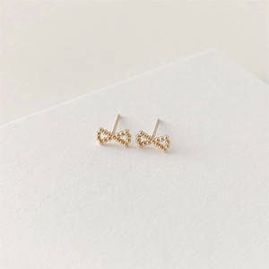 Close-up of golden beaded bow earrings on a minimalist textured cream background