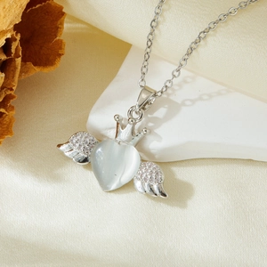 Detailed shot of silver heart necklace with crown wings and opal inlay on fabric