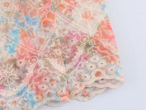 Détail macro du tissu en dentelle tie-dye avec broderie florale blanche et texture ajourée