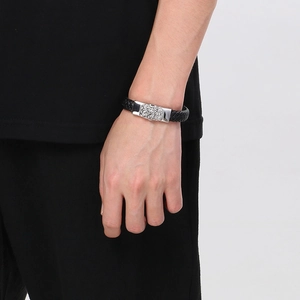 Detail view of men's black braided leather bracelet with silver lion head clasp on wrist