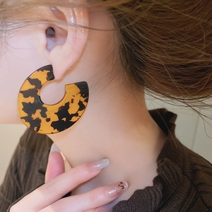 Close-up of large acrylic tortoise shell hoop earring worn by a model in warm tones