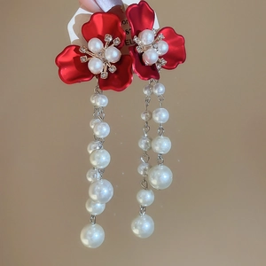 Detailed close-up of red floral earrings with pearls and rhinestones on beige background