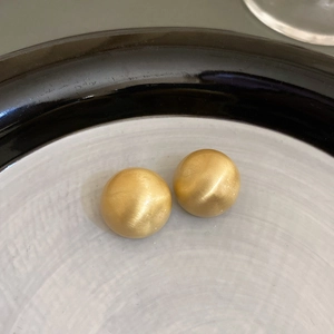 Minimalist matte gold ball earrings with brushed texture on white ceramic plate