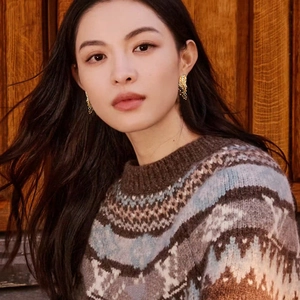Close-up of golden irregular textured earrings worn with a vintage patterned sweater