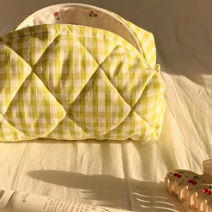 Detail of yellow checkered quilted cosmetic bag with cherry pattern inner lining