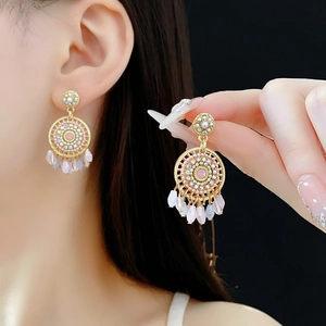 Detail showing golden hoop earrings with pink gemstones and dangling teardrop beads