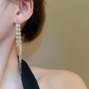Detail of long gold tassel earrings with crystals worn by a model in soft lighting