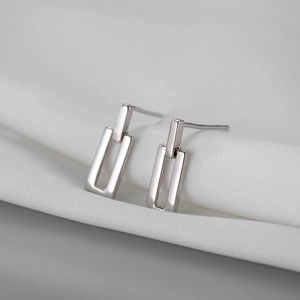 Macro shot of minimalist geometric rectangular S925 silver stud earrings on white fabric