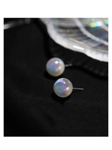 Macro shot of iridescent mermaid pearl studs on black textured fabric and glass