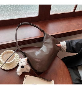 Detail of dark brown leather underarm bag with a plush puppy charm on a wooden table