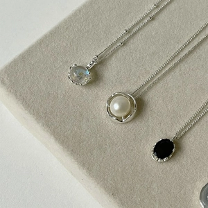 Elegant pearl and gemstone heart pendant necklaces with silver chains on grey surface