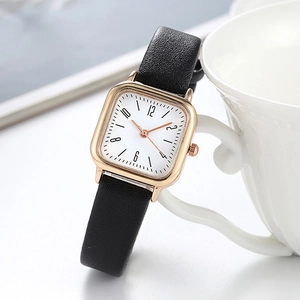 Detail of square rose gold watch with black leather strap next to a white ceramic cup