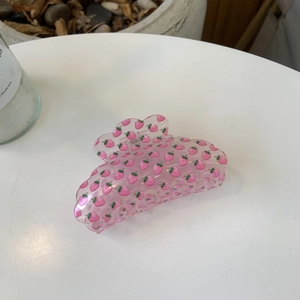 Pink transparent hair claw clip with red strawberry patterns on a white table