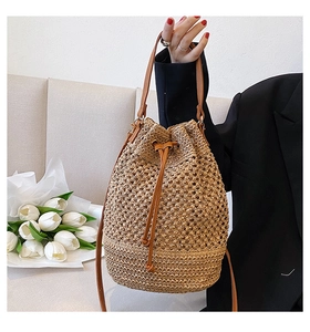 Detail of khaki straw bucket bag with drawstring closure and brown leather shoulder strap