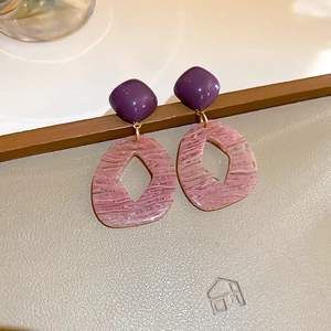 Detail of geometric resin earrings showing purple textured rhombic pendants and gold links