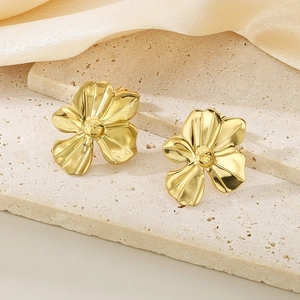 Detail of gold ginkgo leaf earrings on beige stone base with soft silk background