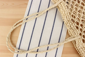 Macro detail of hand-woven beige straw bag featuring mesh texture and sturdy handles