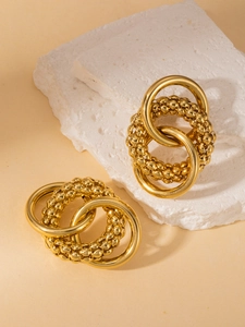 Detailed view of layered gold chain-style hoop earrings on a textured stone surface