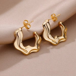 Detail of wavy C-shaped gold earrings placed on champagne silk fabric background