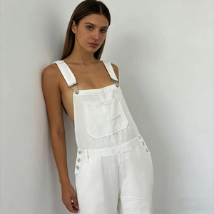 Detailed view of silver metal buckles and side buttons on white denim overalls for women
