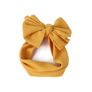 Detailed close-up of a mustard yellow bow headband with textured fabric on white background
